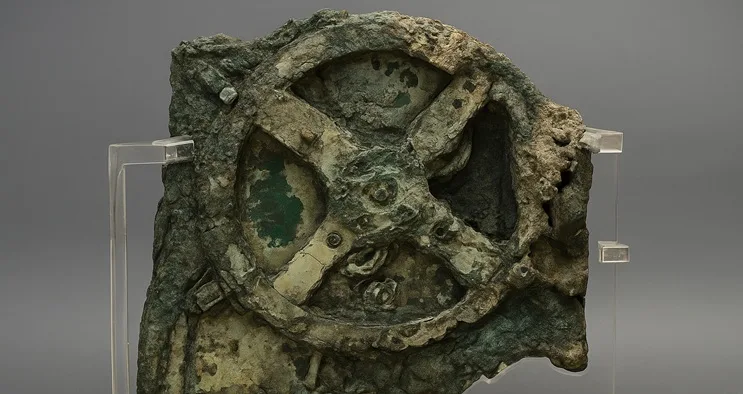 Primer plano del mecanismo de Anticitera, una máquina antigua de engranajes de bronce iluminada sobre fondo oscuro